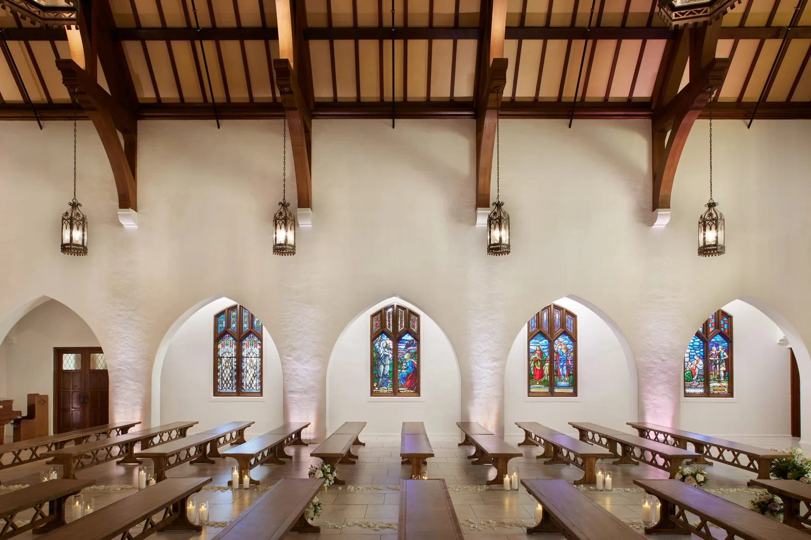 Chapel interior with stained glass windows, wooden pews, hanging lanterns, and floral decorations