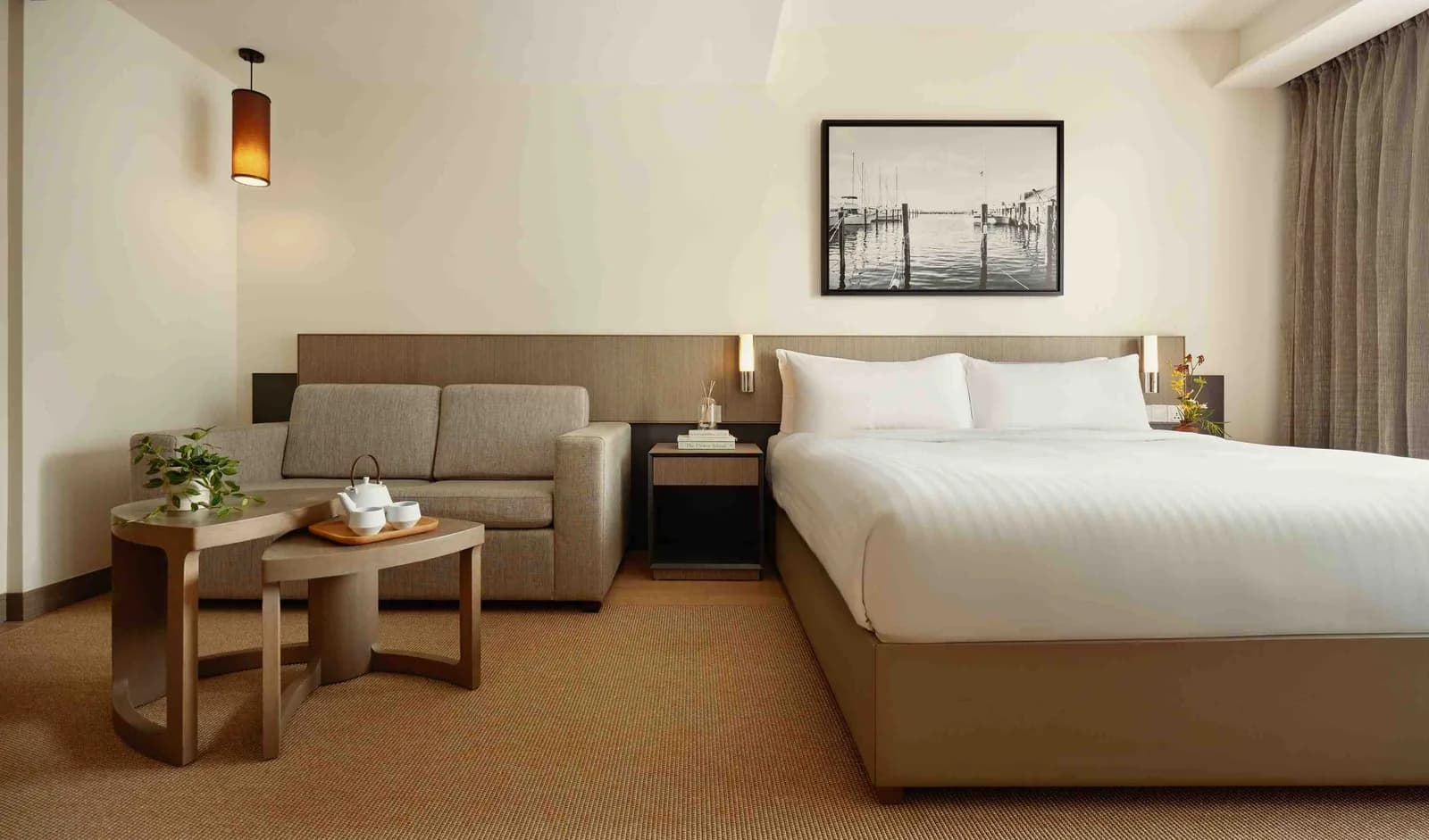 Spacious hotel suite with bed, sofa seating area, and contemporary furnishings in warm neutral tones