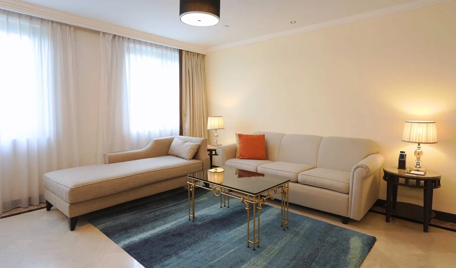 Hotel suite living area with cream sofas, glass coffee table, windows and warm lighting