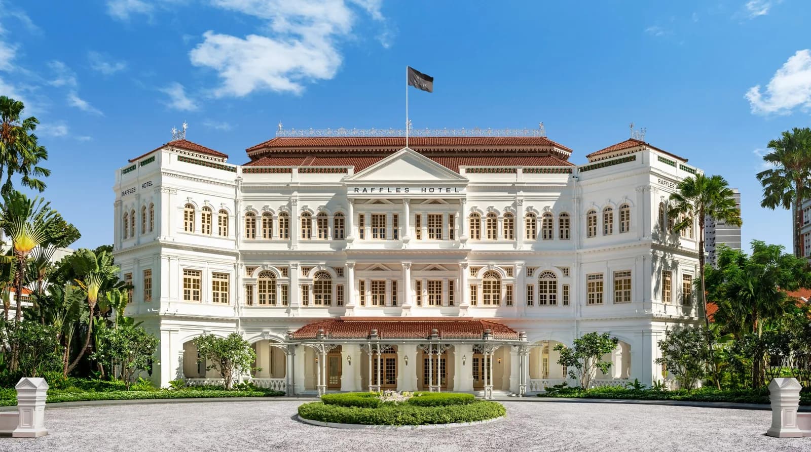 Raffles Hotel's grand white neoclassical facade with red-tiled roofs, palm trees, and manicured courtyard