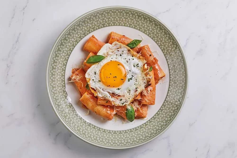Penne pasta with fried egg, basil garnish on green-rimmed white plate