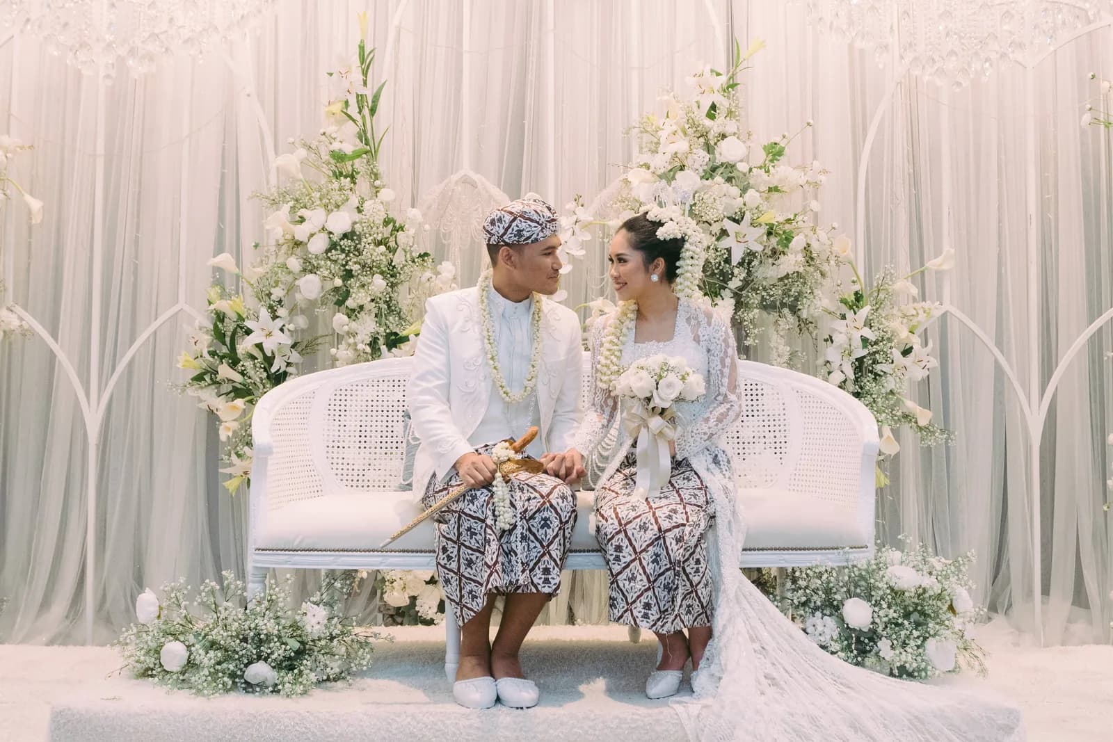 Wedding ceremony setup with white sofa, elaborate floral arrangements, and draped backdrop