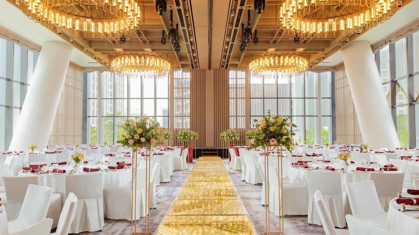Luxury wedding ballroom with round tables, gold lighting, and tall windows