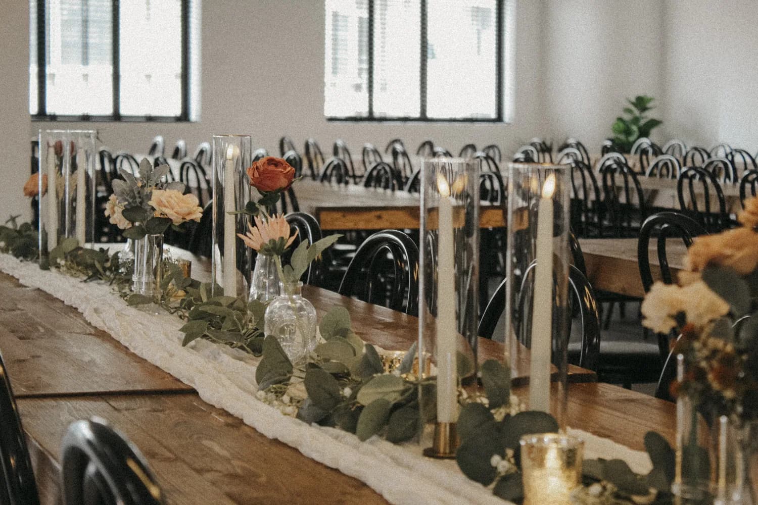 Wedding reception table with floral centerpieces, candles, and greenery in a bright banquet hall