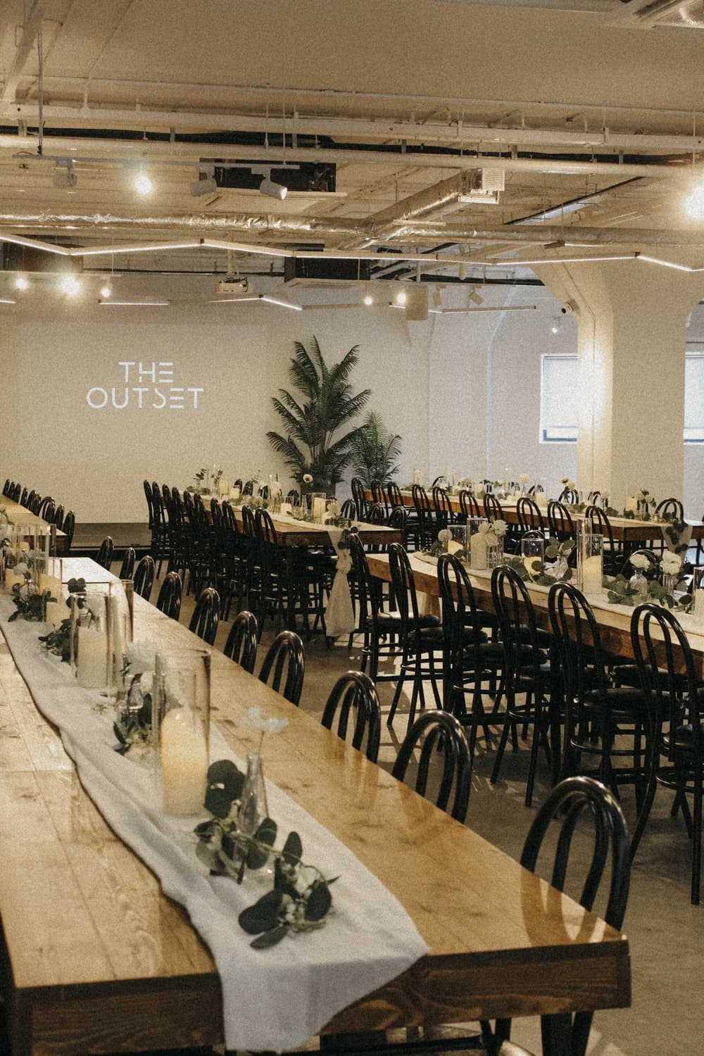 Modern event venue with long dining tables, black chairs, and contemporary decor under industrial ceiling