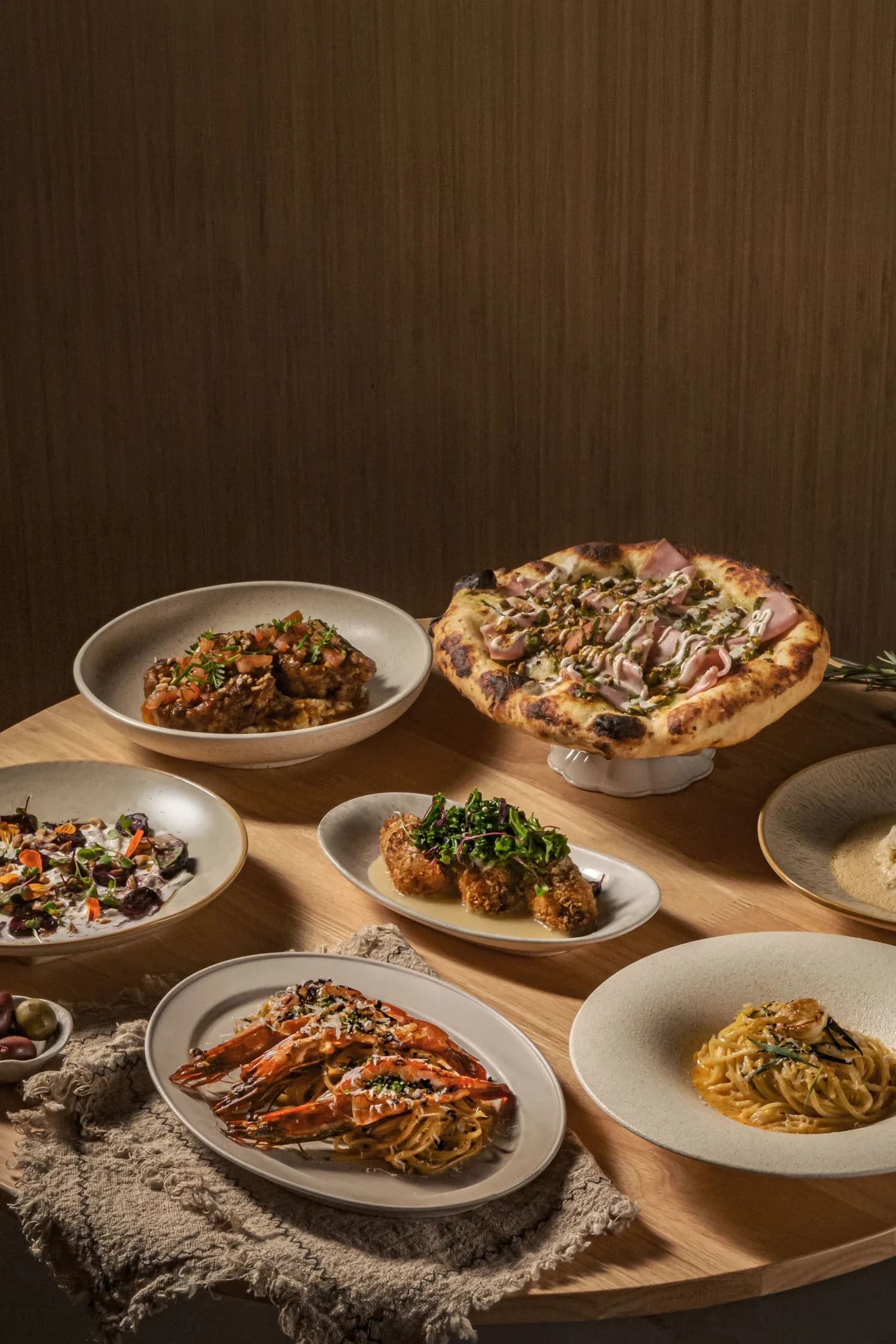 Italian dishes including pasta, pizza with ham and greens, lobster, and appetizers on white plates