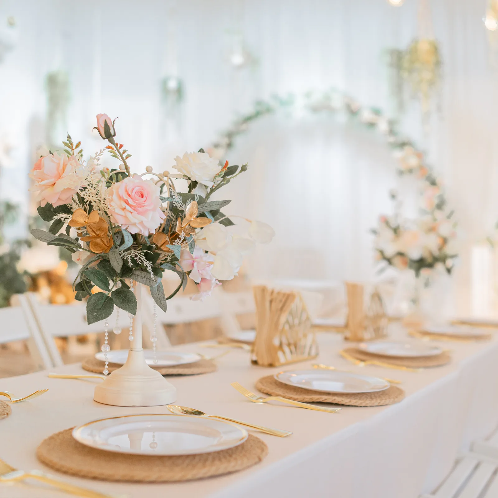 Wedding table setting with pink flower arrangement, white plates, and gold accents in a bright venue.