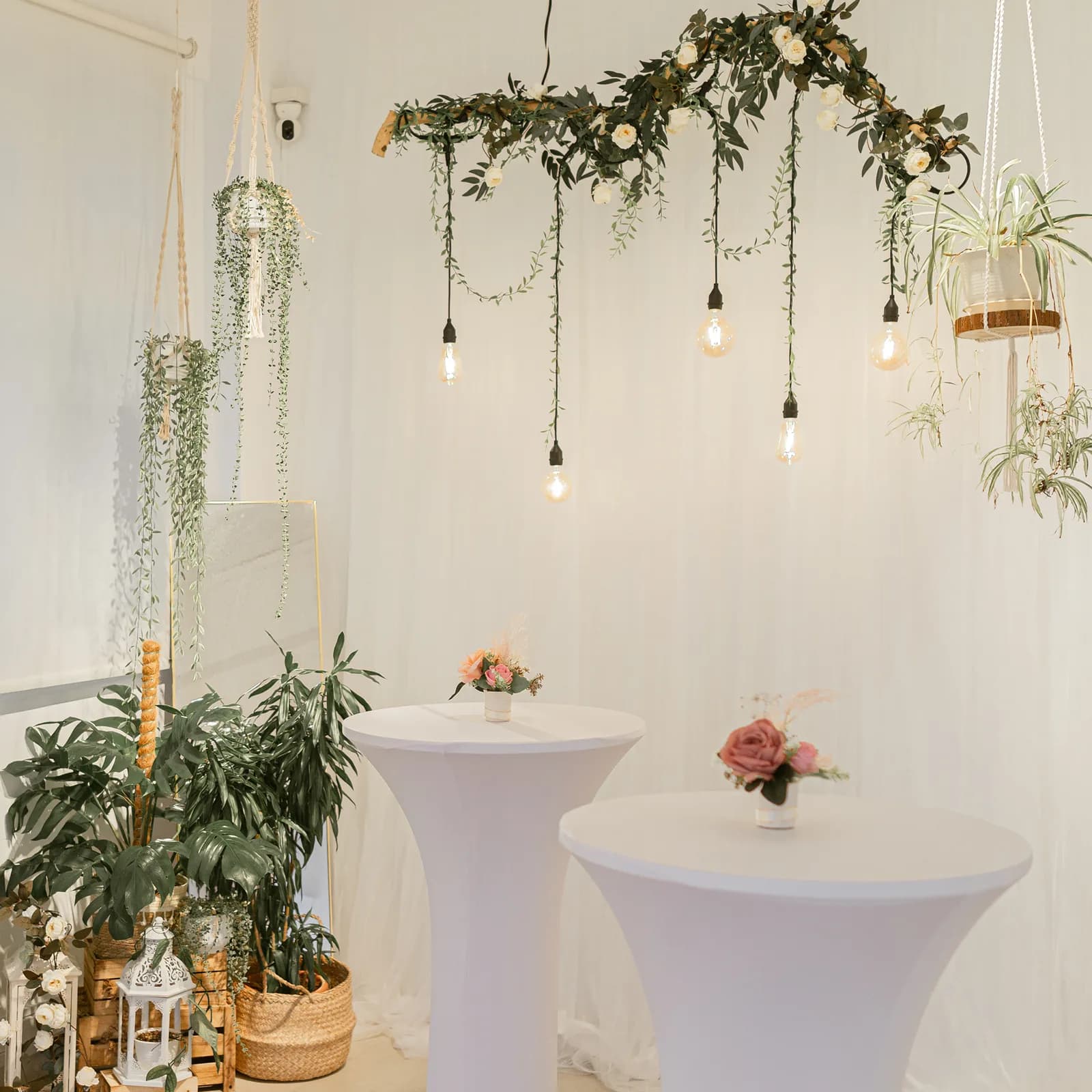 Wedding venue setup with draped greenery, hanging lights, and white tables decorated with flowers
