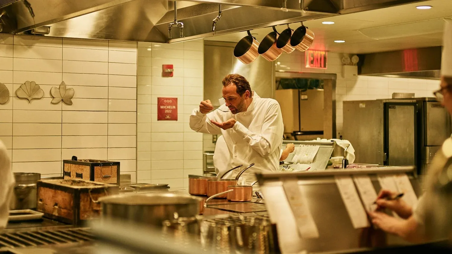 Chef cooking at stove in modern open kitchen with hanging copper pots