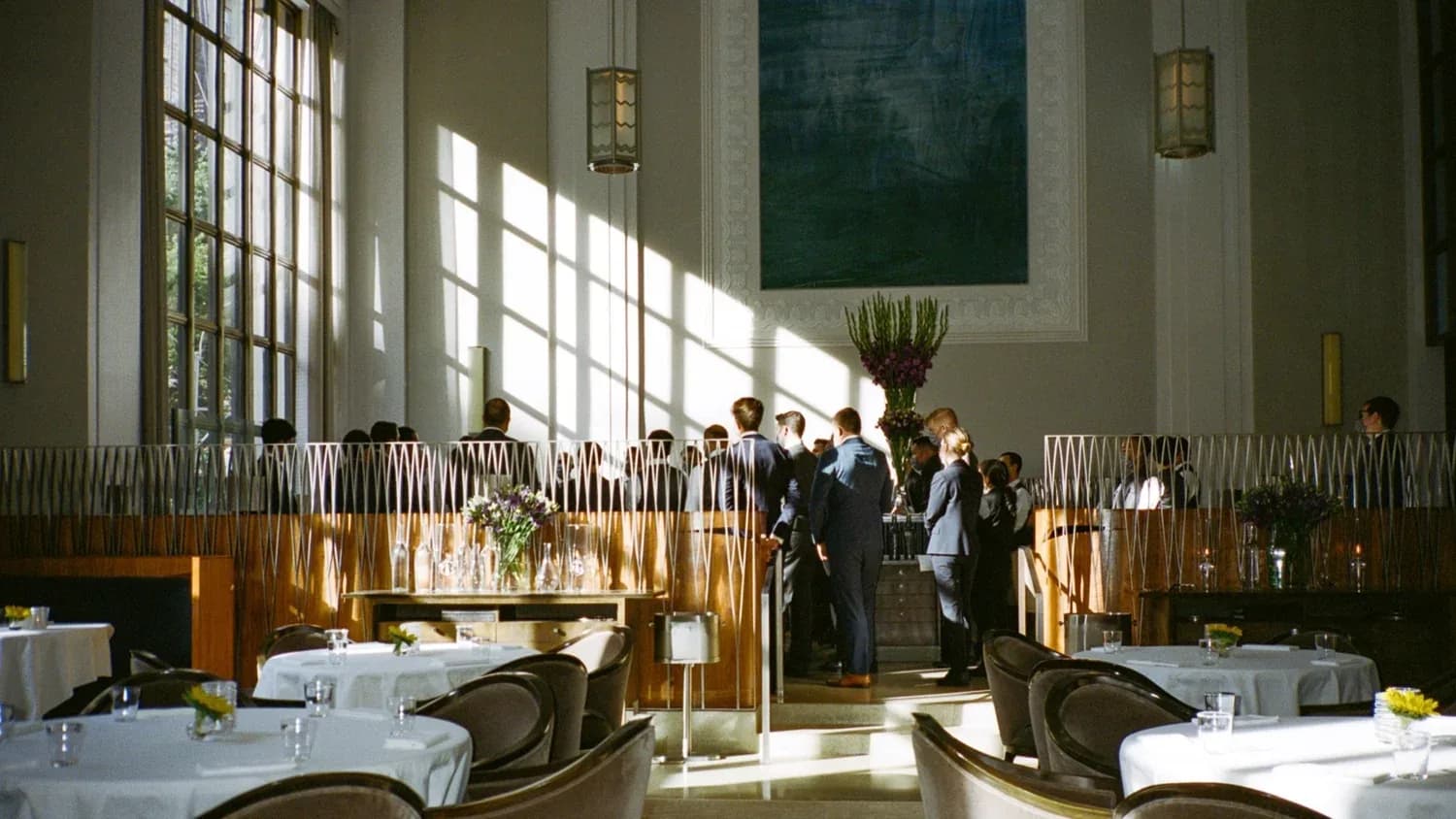 Elegant fine dining room with soaring windows, white tablecloths, and natural light streaming across modern furnishings