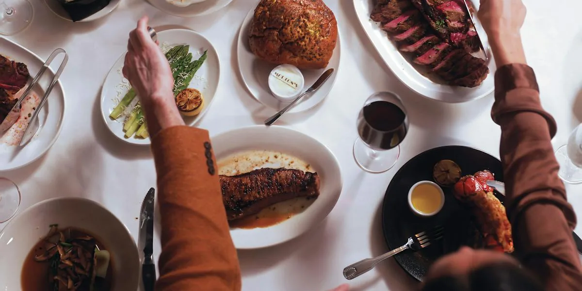 Fine dining steakhouse table with seared steaks, grilled vegetables, and wine glasses