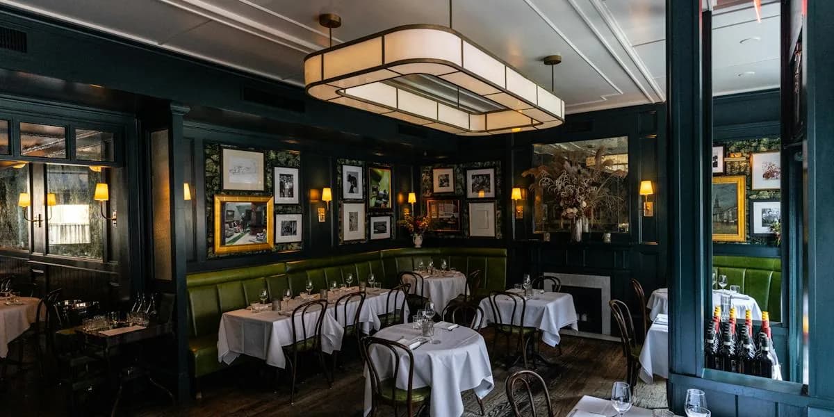 Sophisticated restaurant dining room with green banquettes, white tablecloths, and gallery wall of framed photographs