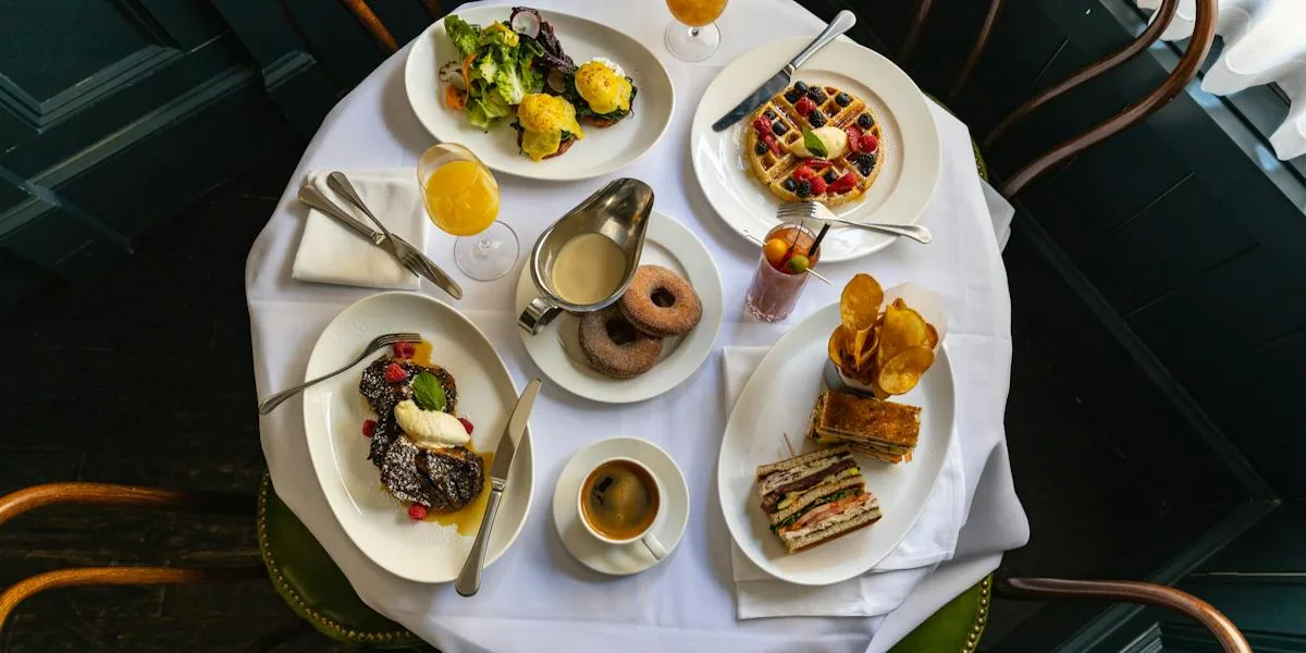 Overhead view of restaurant table with various plated breakfast dishes, drinks, and desserts