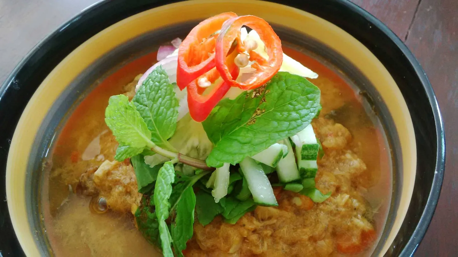 Bowl of spiced curry soup with meat, mint, chili, and onion garnish
