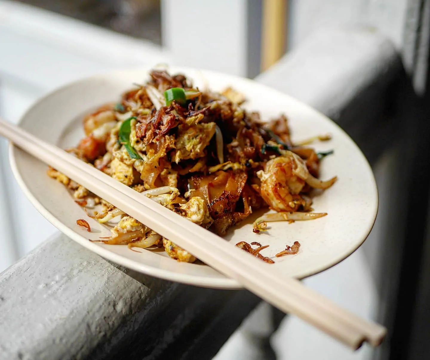 Crispy fried noodle dish with green garnish and chopsticks on white plate