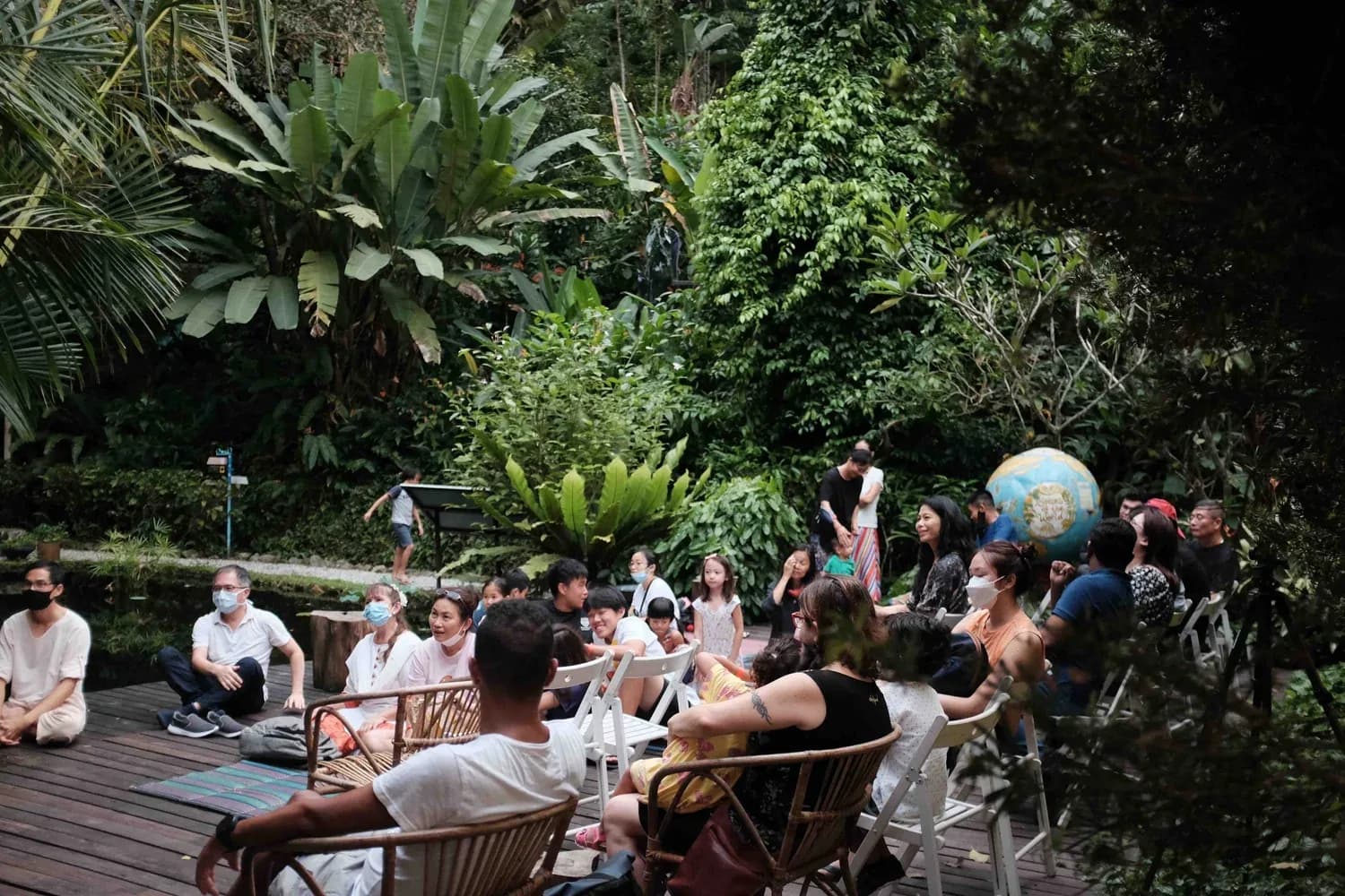 Guests seated on a wooden deck in a verdant tropical garden venue with dense foliage surrounding the space.