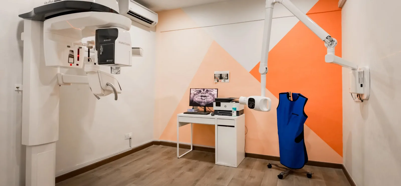 Dental clinic treatment room with imaging equipment, workstation, and modern orange and white design