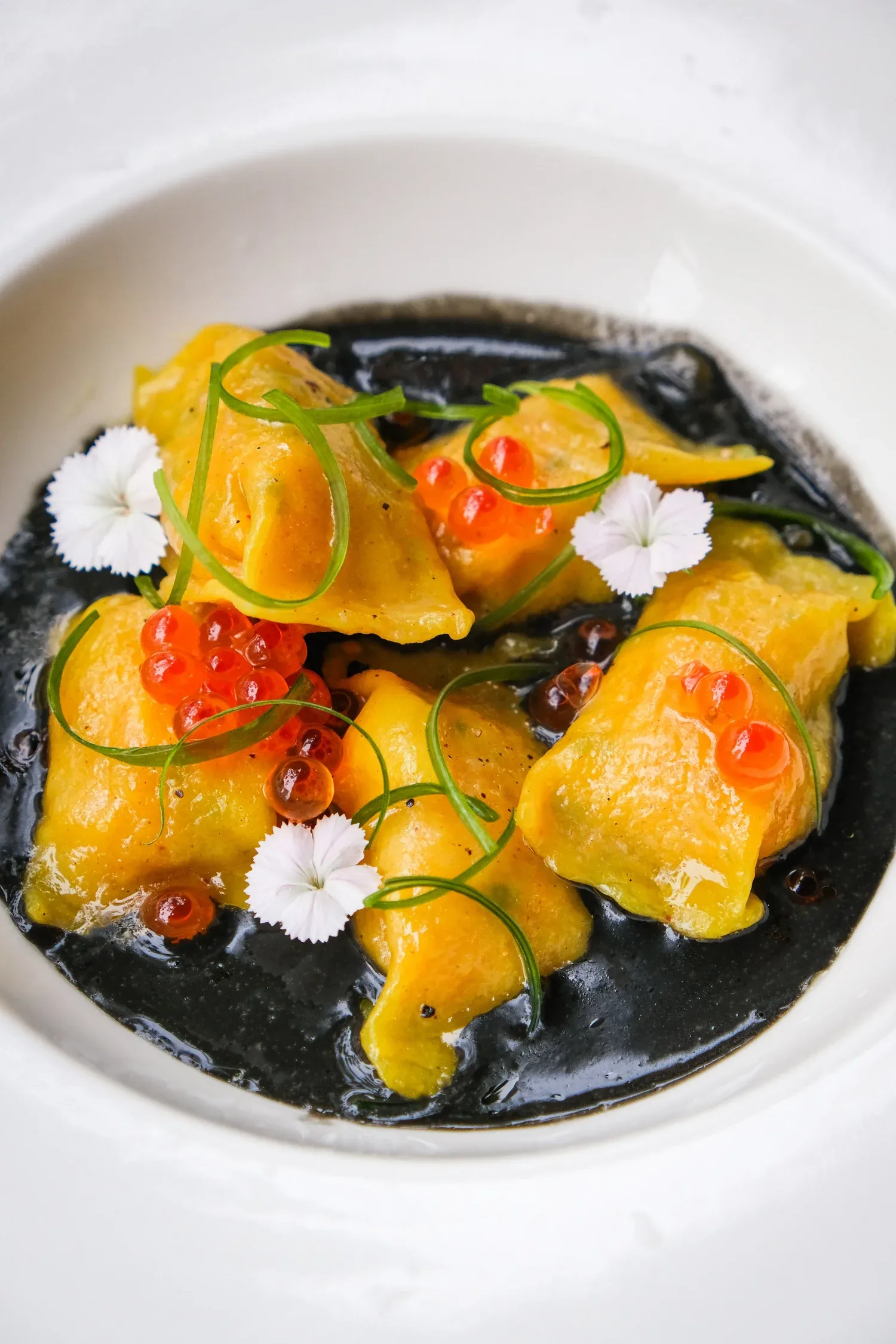Golden pasta with squid ink sauce, topped with chives, red roe, and edible flowers
