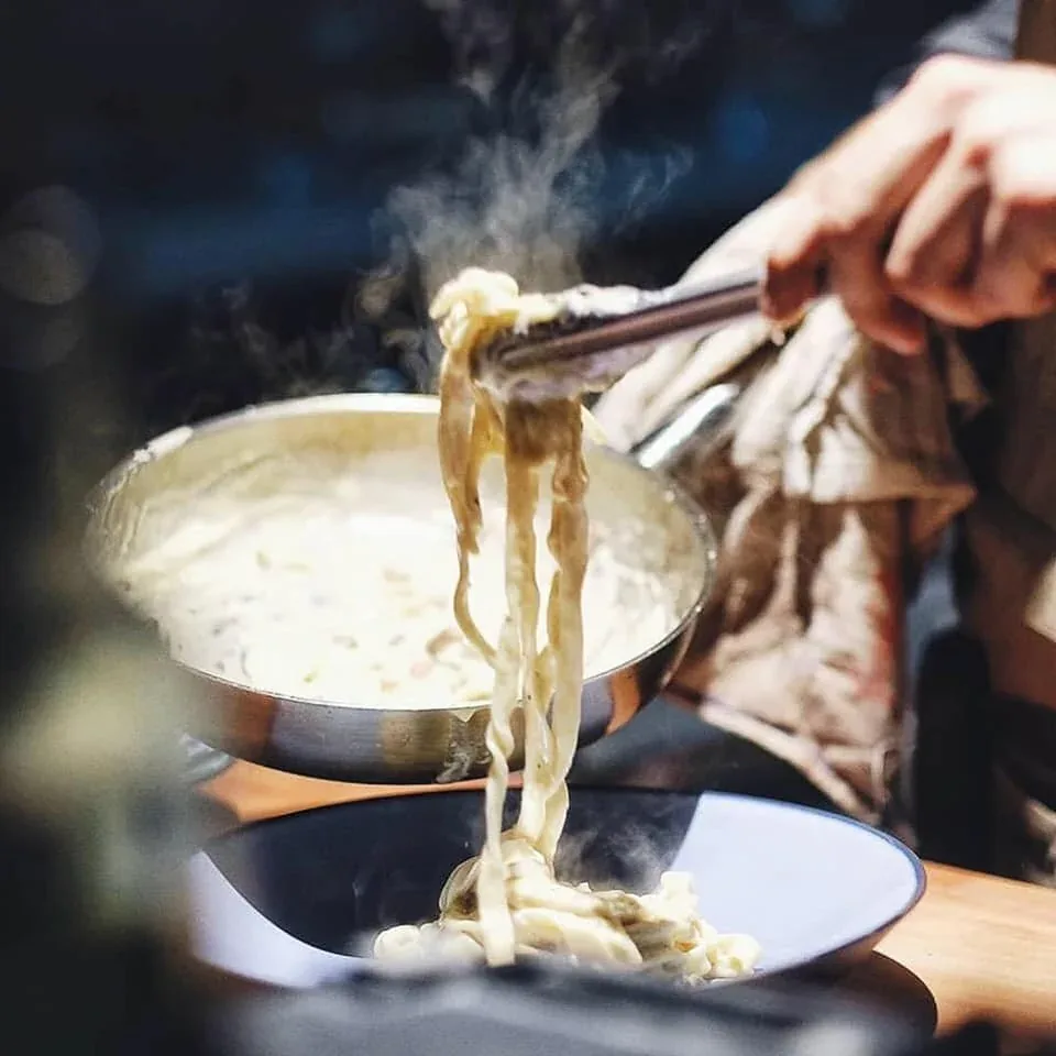 Chopsticks lifting steaming noodles from a creamy pasta dish
