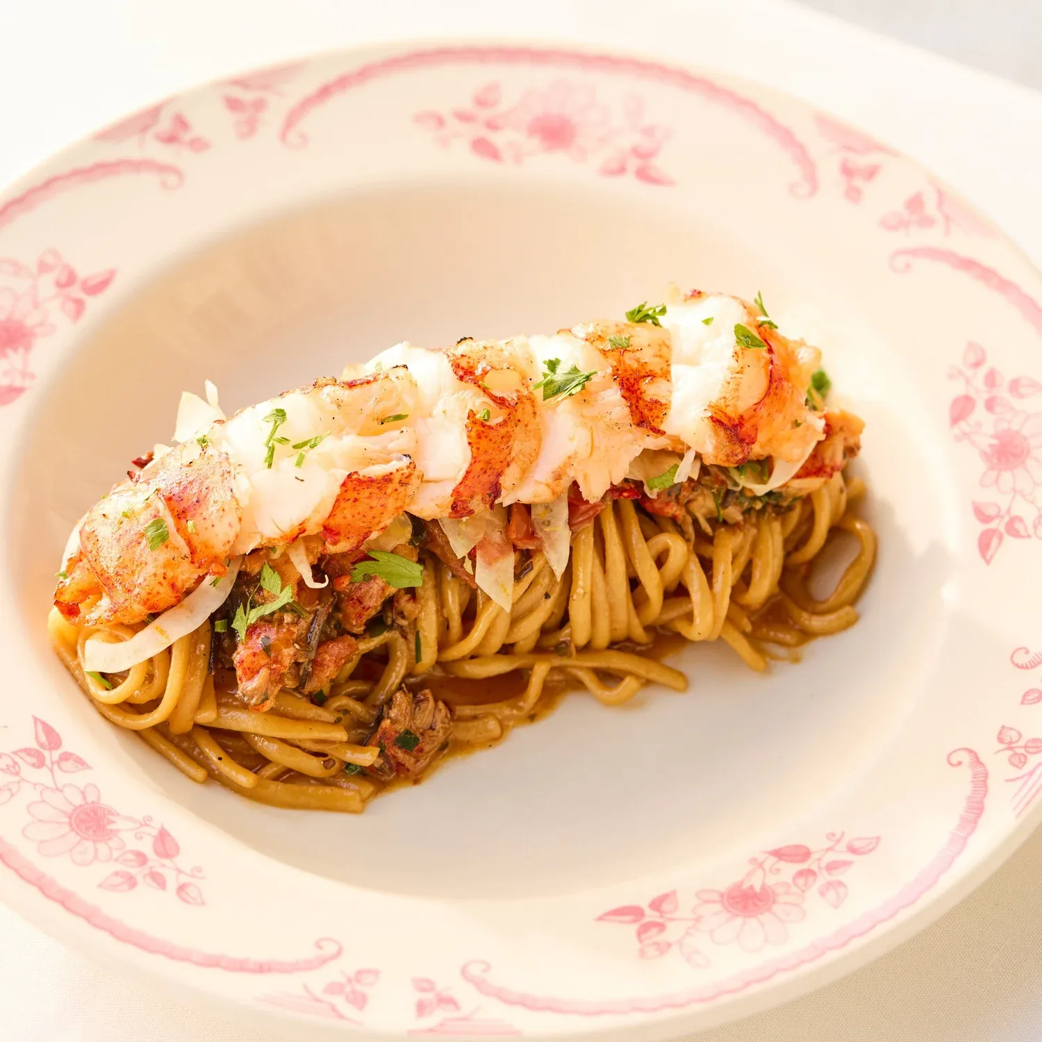Seared seafood pasta with creamy sauce and herbs on a pink-rimmed plate