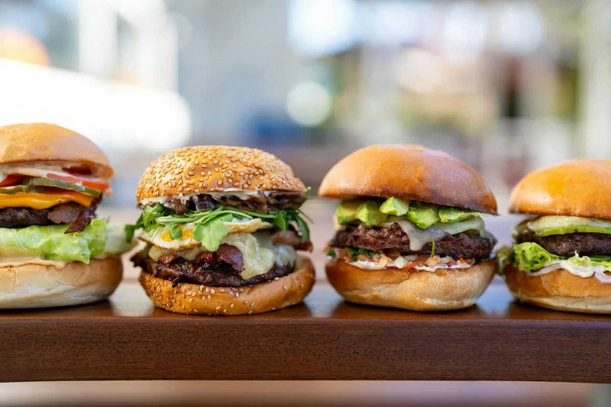 Four specialty burgers with different toppings arranged on a wooden board.
