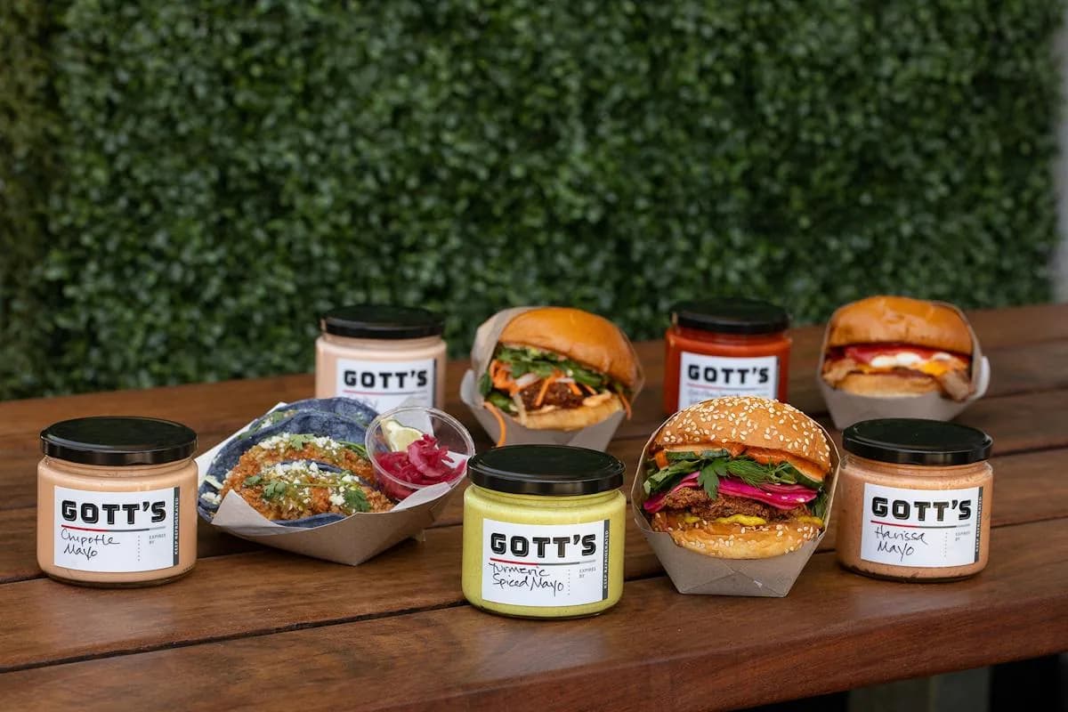 Gott's burgers, sauces in jars, and a bowl of prepared dish on wooden display table