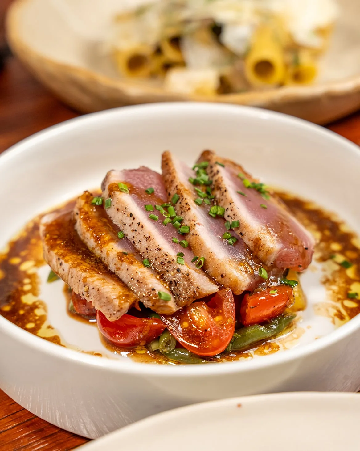 Sliced duck breast with crispy skin, green garnish, and roasted vegetables on white plate