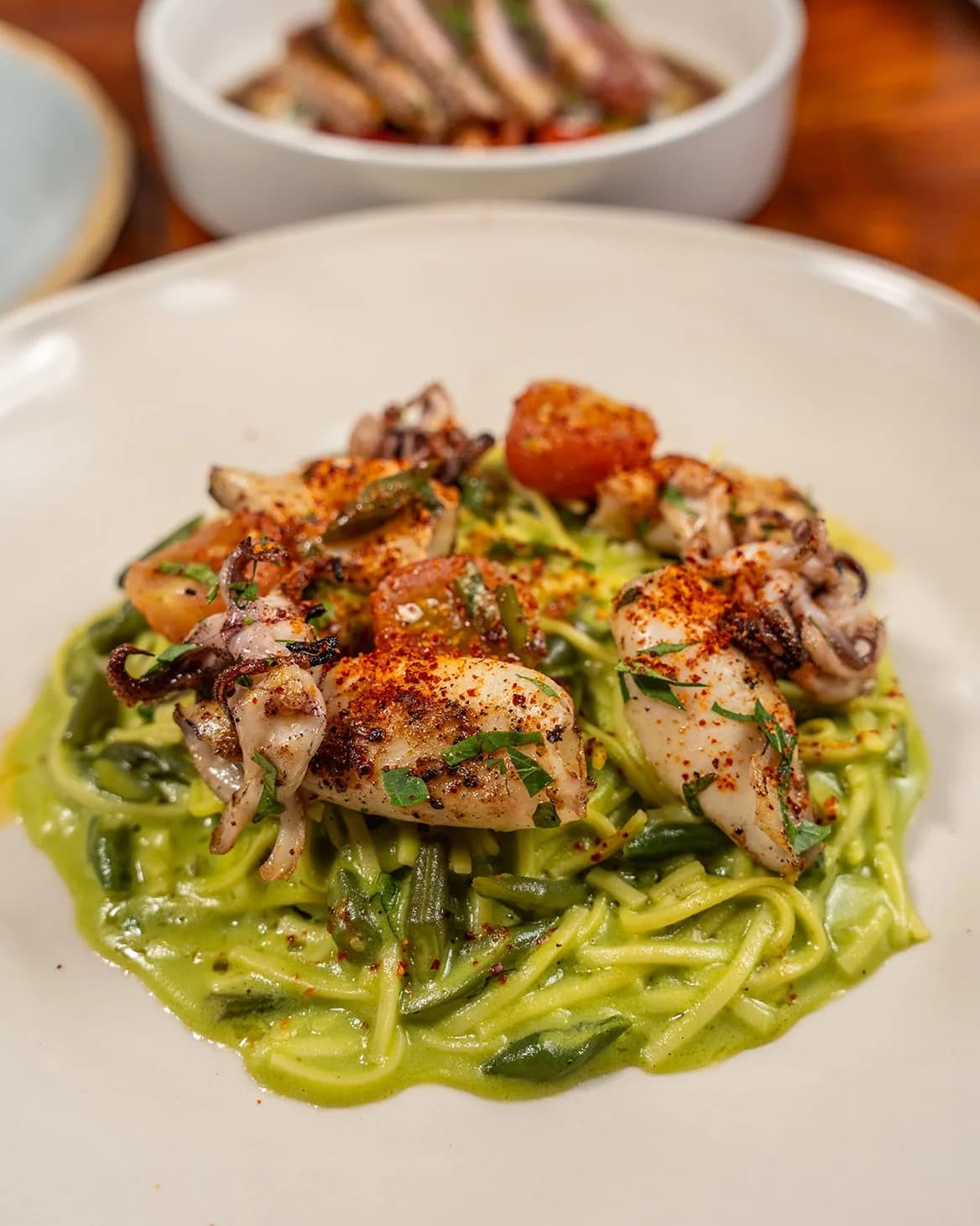 Seared squid with green pasta, herbs, and spice on a white plate