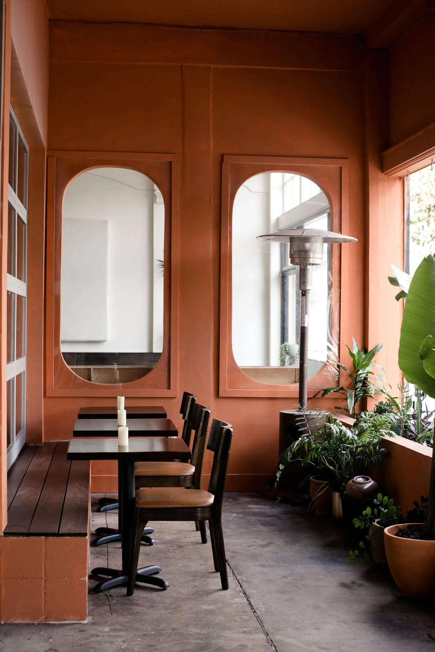 Warm terracotta dining room with black table, chairs, arched windows, and potted plants