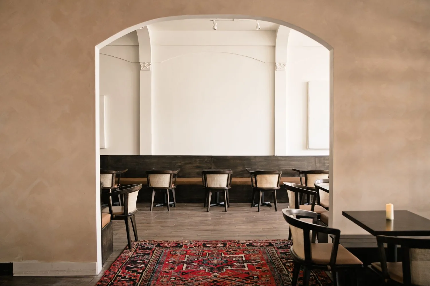 Modern restaurant dining room with arched architectural details, banquette seating, and decorative red rugs.