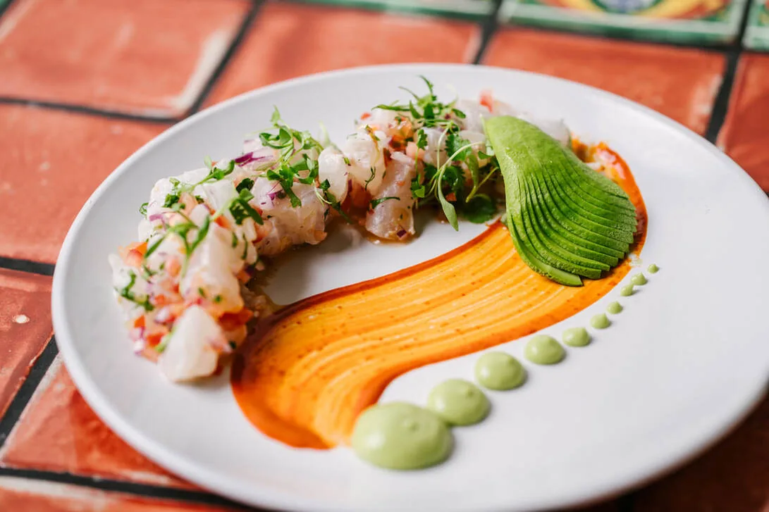 Elegantly plated sushi roll with microgreens, avocado, and orange sauce on white plate