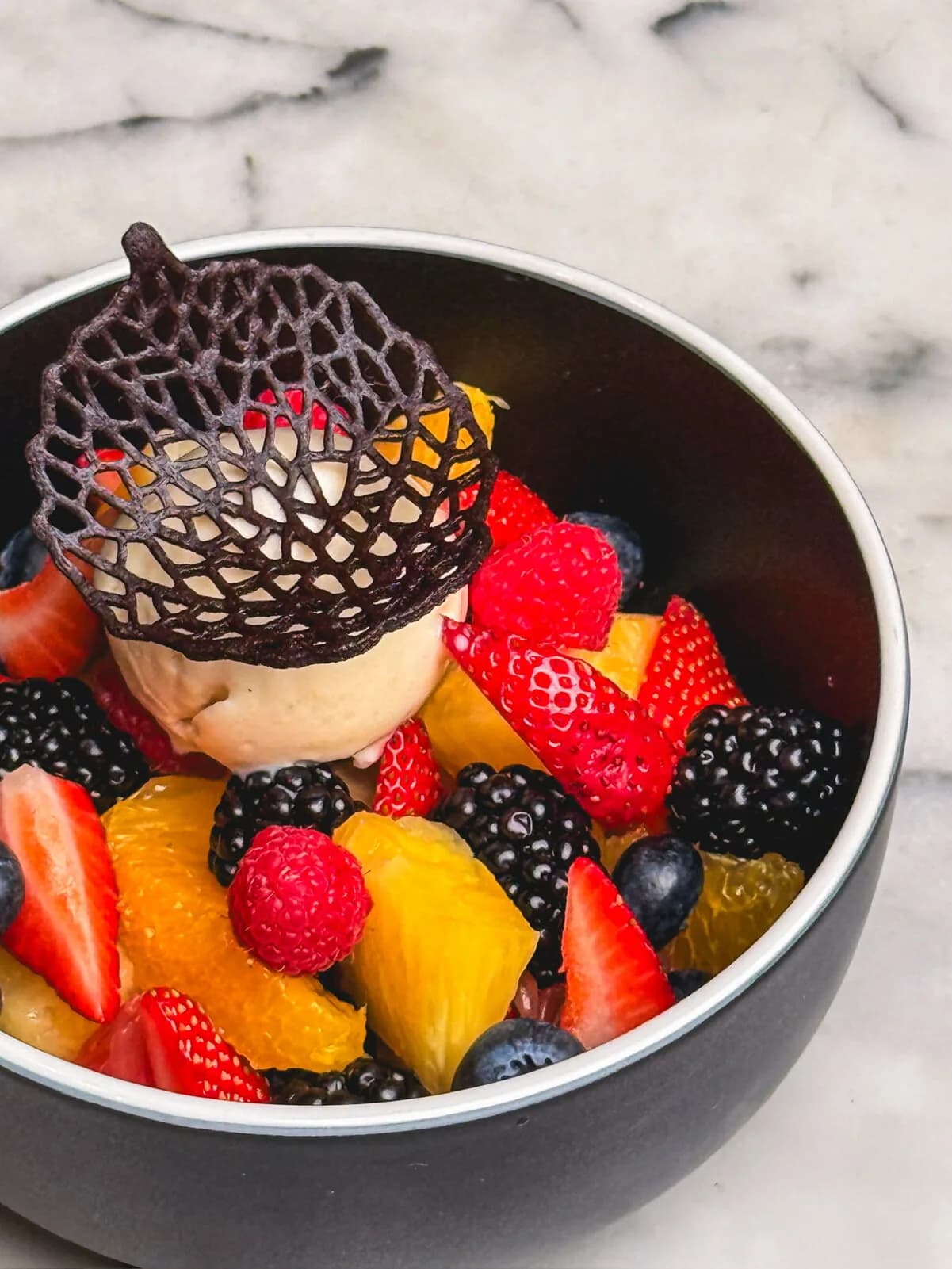 Colorful dessert bowl with fresh berries, mango, cream, and chocolate web garnish