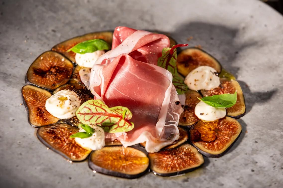 Plated dish with prosciutto, mozzarella, roasted figs, and fresh basil on gray surface