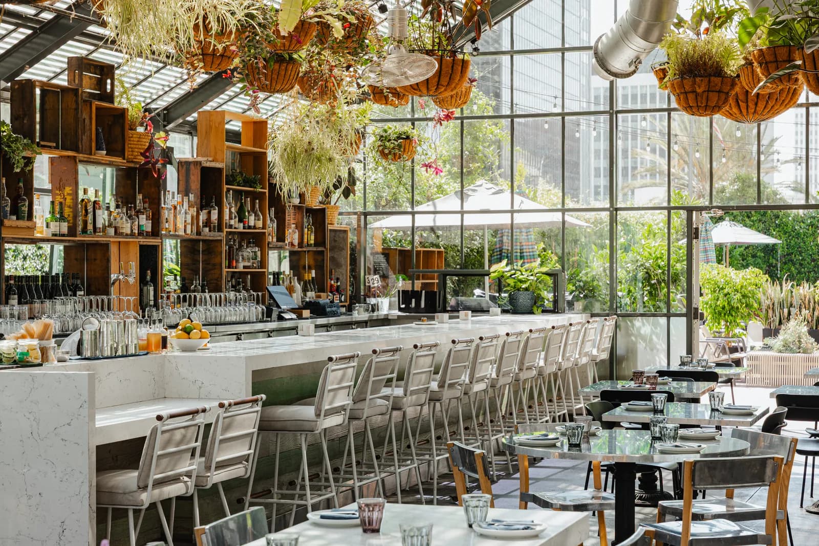 Modern restaurant interior with bar seating, hanging plants, and garden views