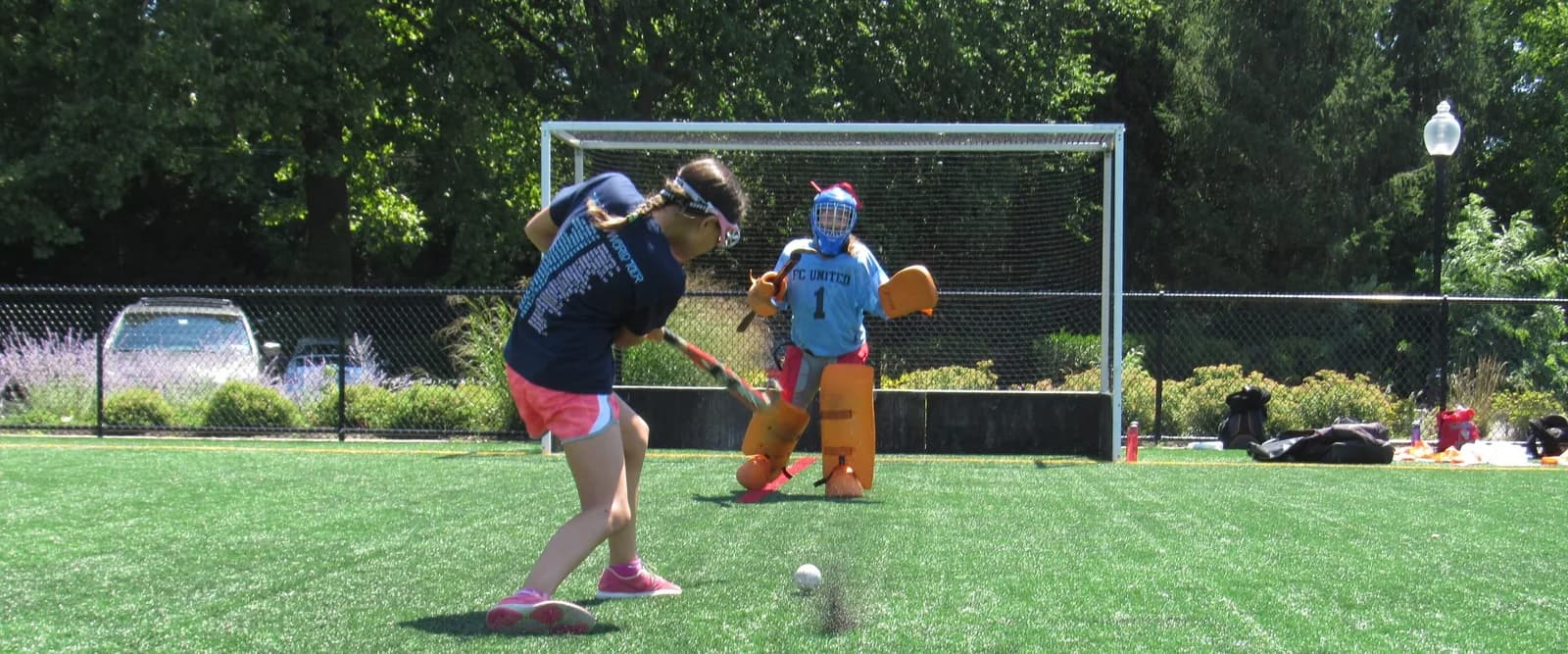 Girl swinging bat at baseball during camp, with catcher and dugout in background