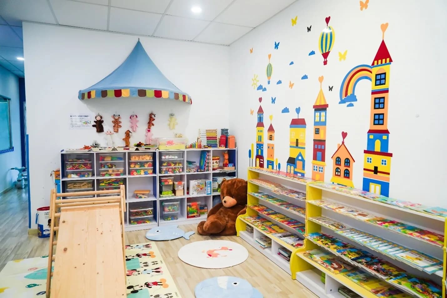 Colorful preschool classroom with castle wall mural, toy storage units, bookshelves, and play equipment