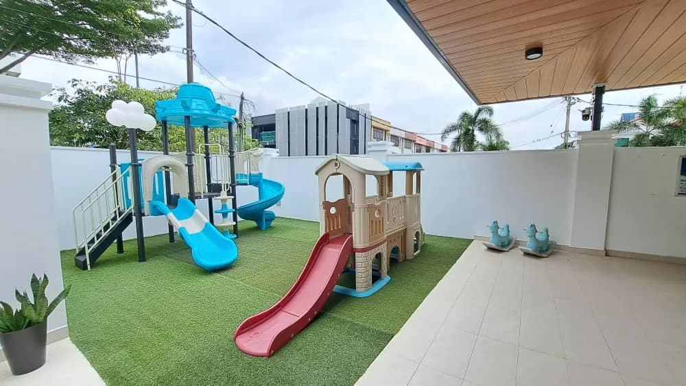 Outdoor playground with blue and pink slides, climbing structures, and artificial grass at preschool