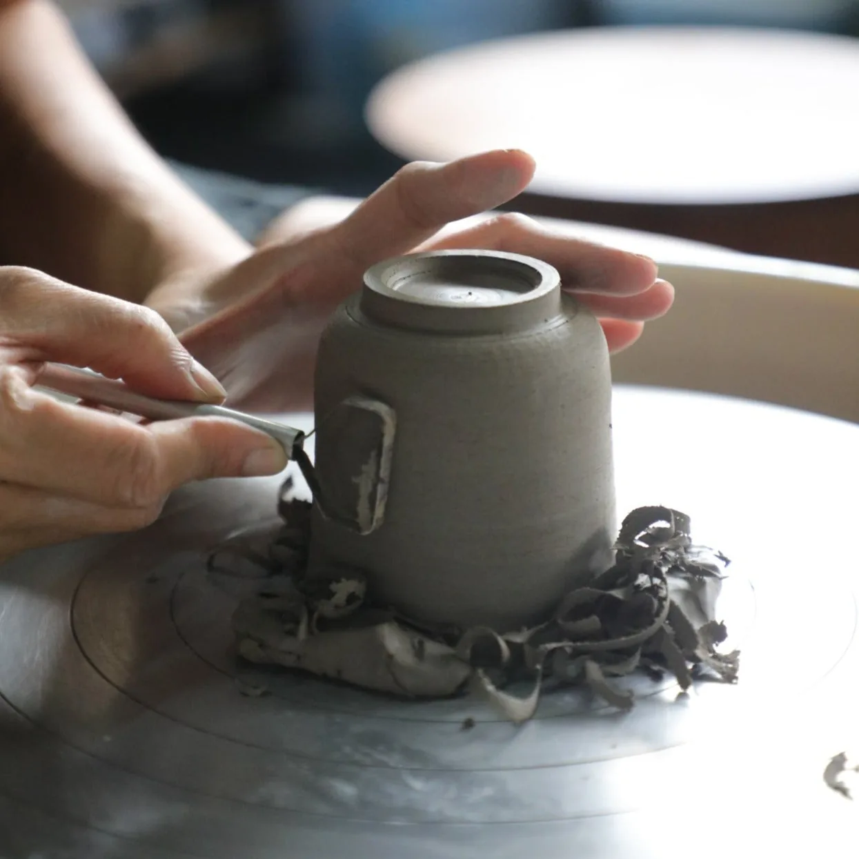 Hands holding a gray ceramic pot with organic base decoration on a plate