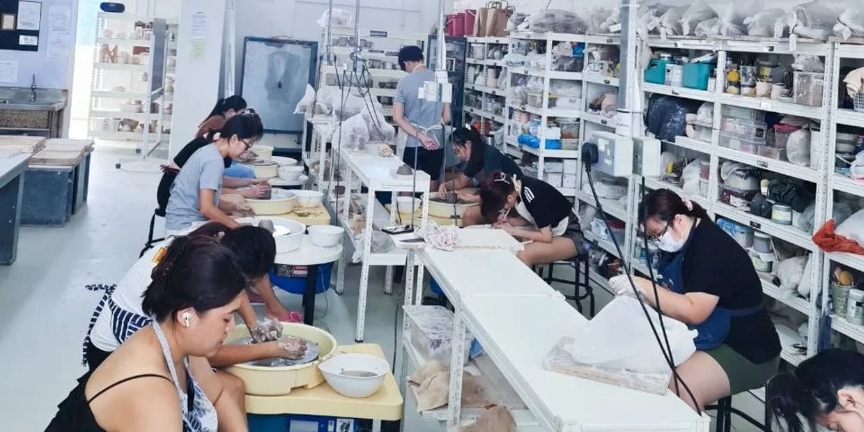 Ceramics studio with students working at tables surrounded by shelves of pottery supplies