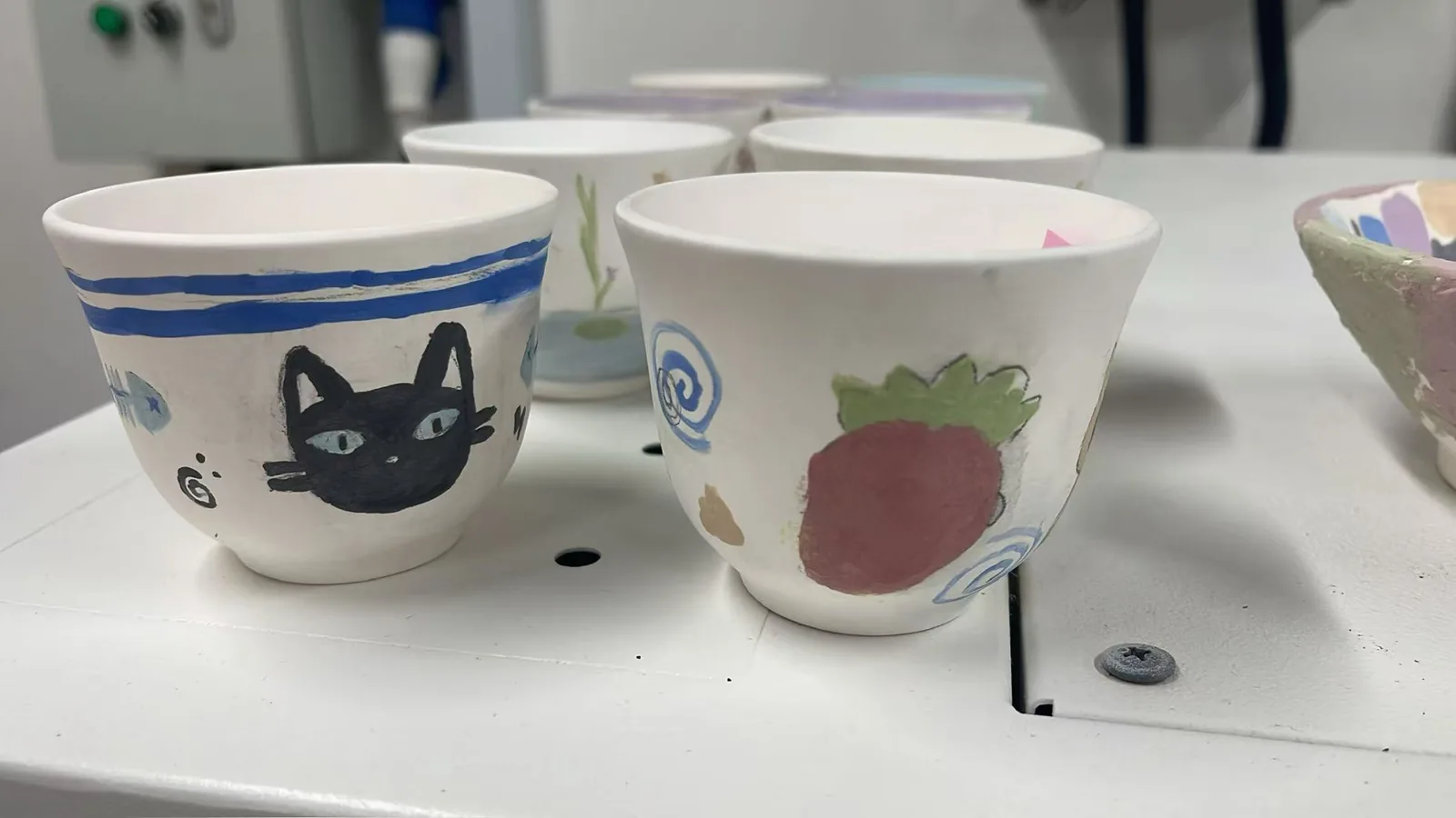 Hand-painted ceramic bowls with cat and strawberry designs on white table