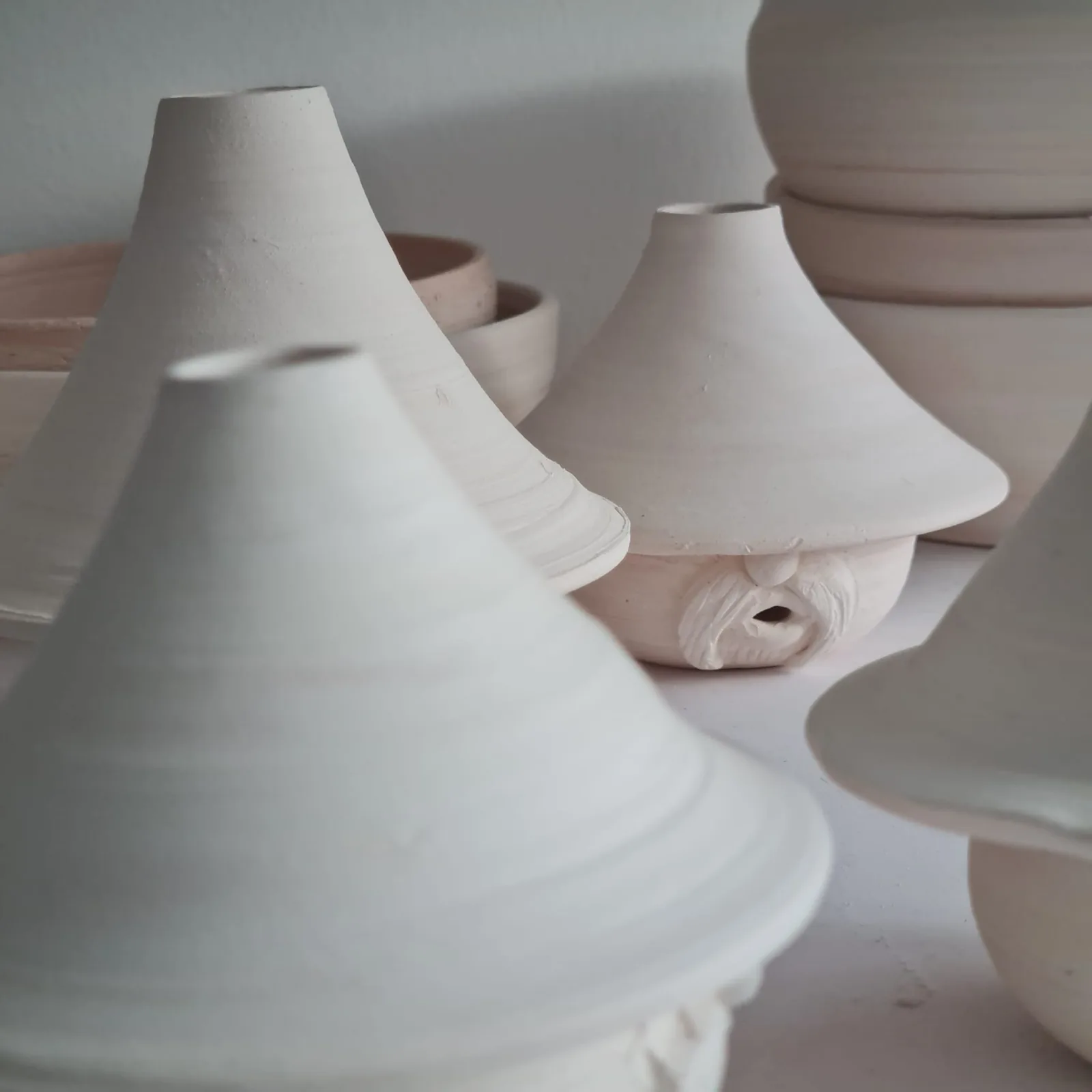 White ceramic vessels with conical and organic shapes arranged on a wooden surface