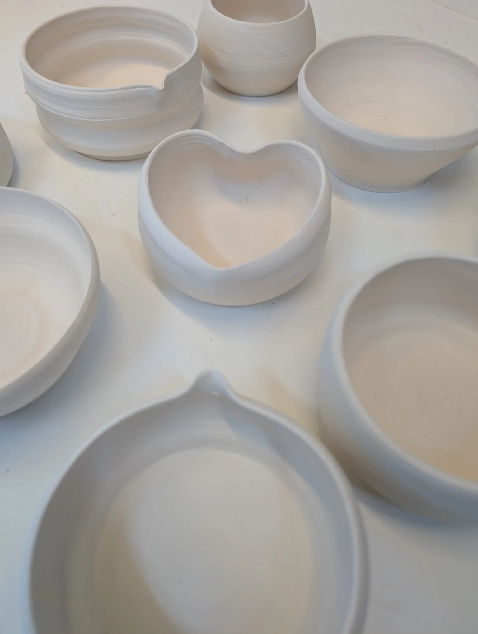 Handmade white ceramic bowls and vessels with a heart-shaped dish displayed on a surface