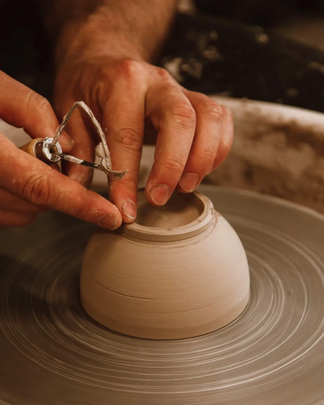 Potter's hands shaping clay on a wheel with a wire trimming tool