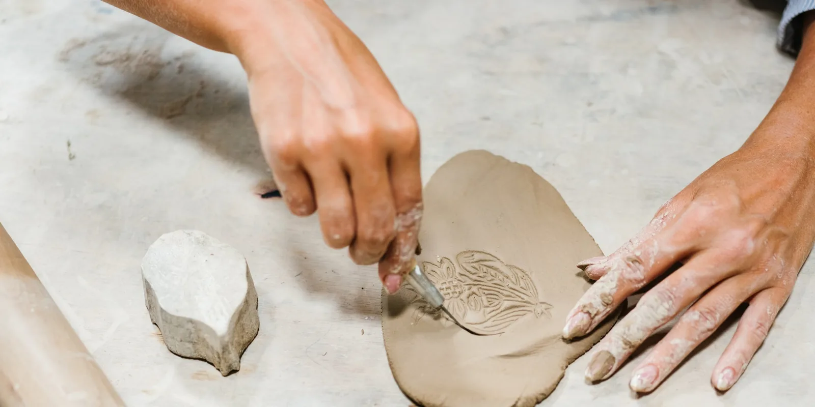 Potter's hands carving ornamental patterns into wet clay on a work table