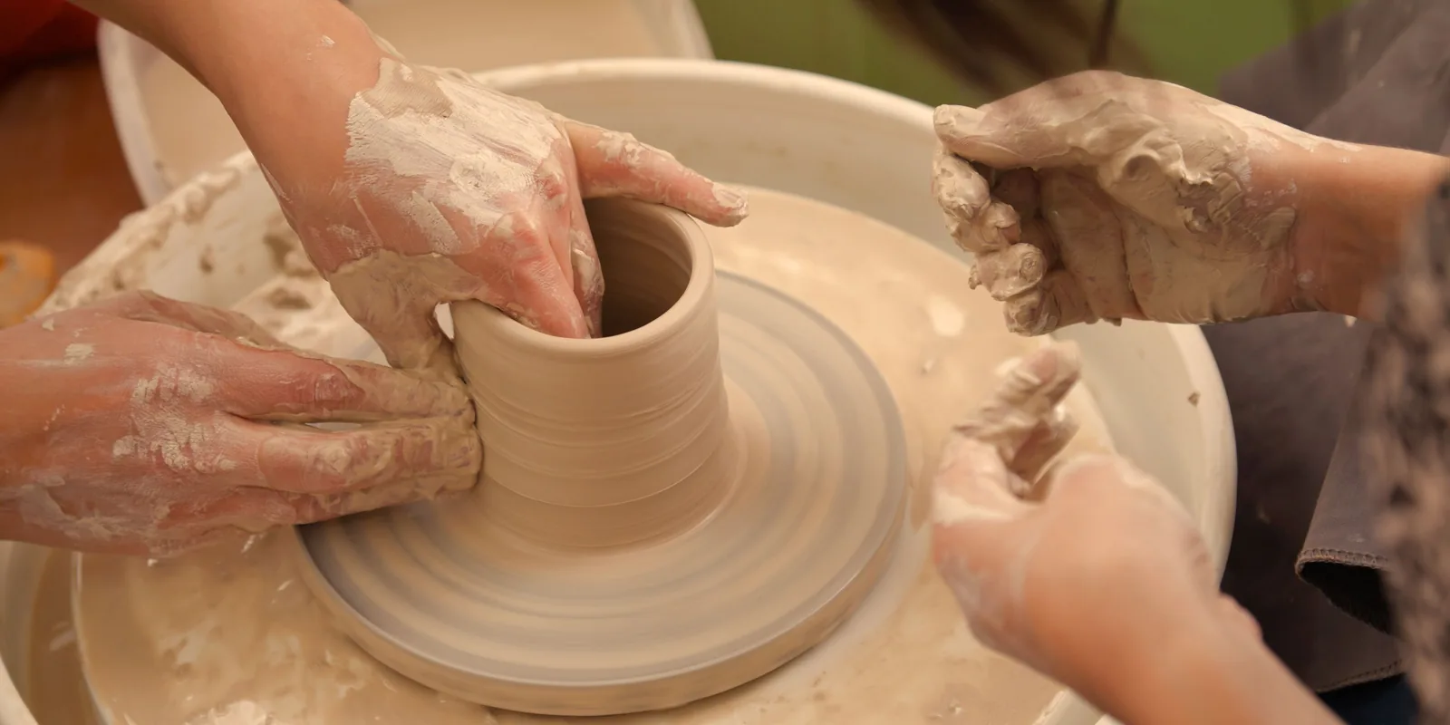 Hands shaping wet clay on a pottery wheel during a collaborative ceramics session