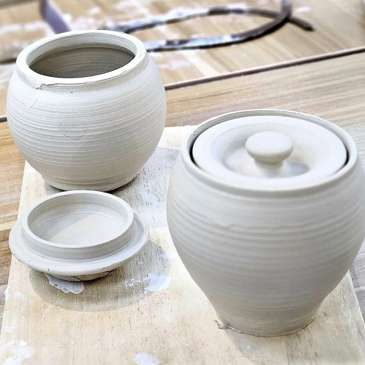 Three white ceramic pots with textured surfaces arranged on wooden board