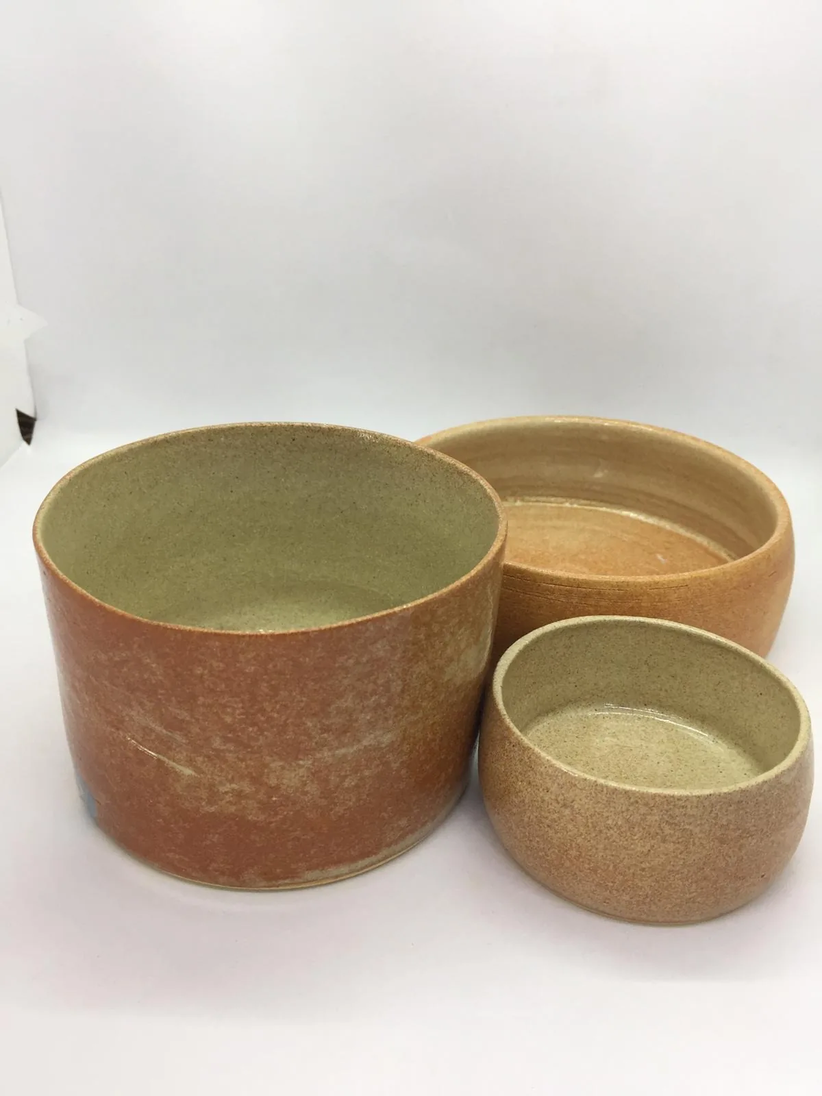 Three ceramic bowls in different sizes with green and natural clay finishes