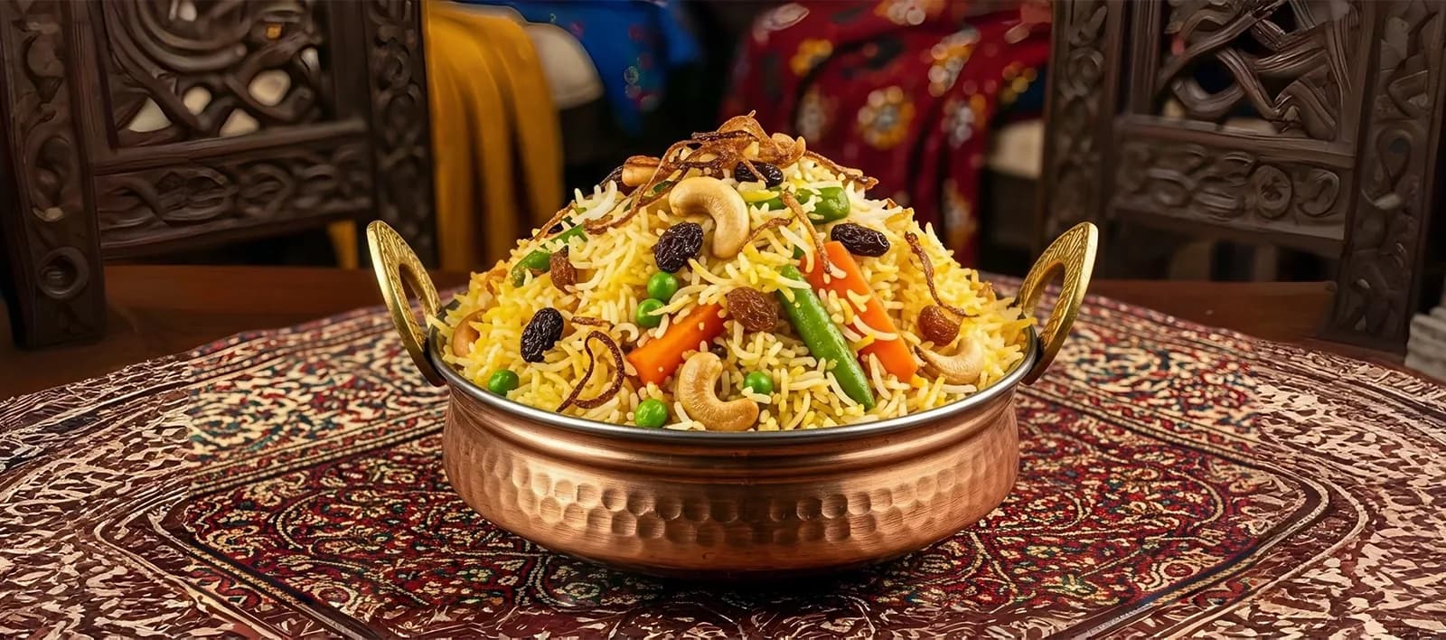 Biryani in a copper handi bowl with cashews, raisins, and vegetables on a patterned table