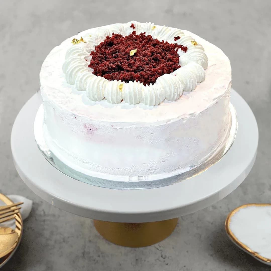 Red velvet layer cake with white frosting and gold leaf garnish on a cake stand