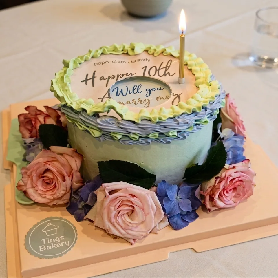 Decorated birthday cake with green and lavender frosting, fresh flowers, and lit candle